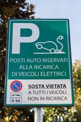 Fototapeta premium Italian road sign indicating parking spaces reserved for electric vehicle charging, with no stopping allowed for non-charging vehicles. Concept of electric mobility and sustainable transportation.