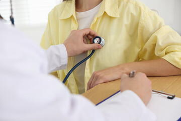 Doctor checking woman's heartbeat with stethoscope in hospital, closeup