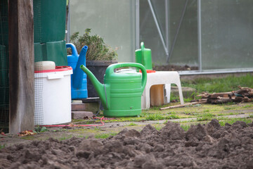 Colorful plastic watering can and garden tools near greenhouse in backyard