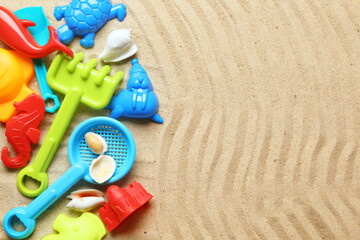 Bright children's beach toys and seashells on sand, flat lay. Space for text