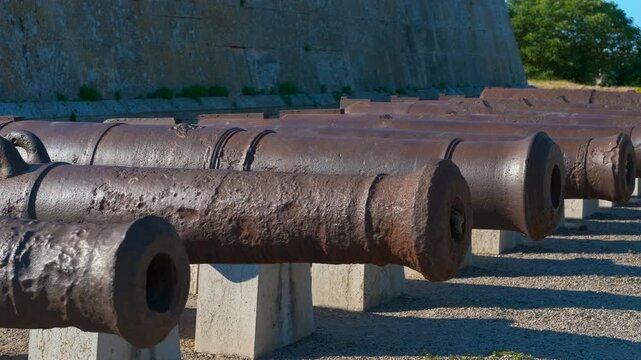 Ancient rusty cannons protecting a historic fortress. Long row of old, rusty cannons lined up on concrete pedestals as a historical display at an ancient military fortification, symbolizing defense