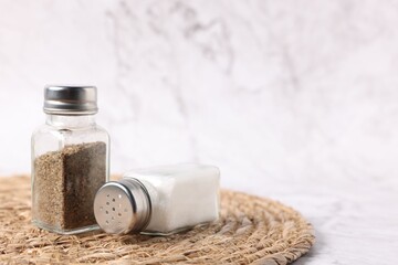 Salt and pepper shakers on white marble background, closeup. Space for text