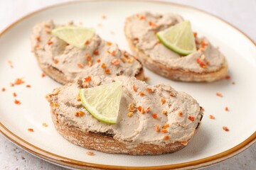 Tasty bruschettas with pate, lemon slices and dried carrot flakes on light table, closeup