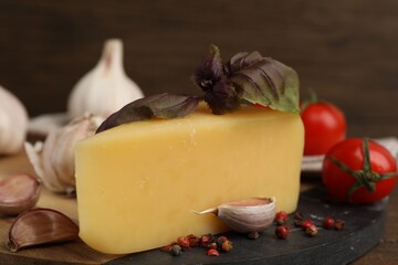 Dairy product. Piece of cheese, tomatoes, basil, peppercorns and garlic on table against brown background, closeup