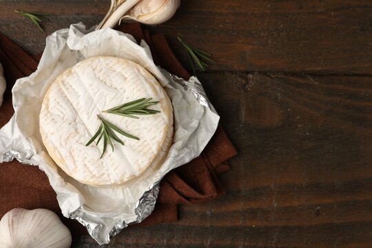 Dairy product. Fresh camembert, rosemary and garlic on wooden table, flat lay. Space for text