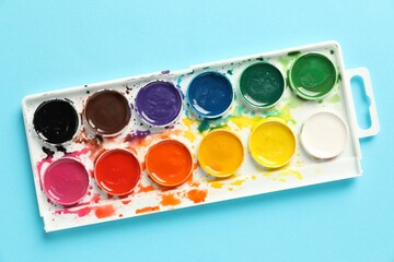Watercolor palette on light blue background, top view
