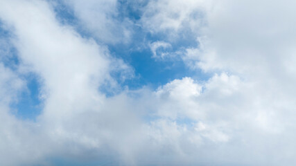 Obraz premium A bright blue sky filled with scattered white, fluffy clouds. The sunlight illuminates the edges of the clouds, creating a peaceful and open atmosphere in the upper atmosphere.