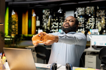 African american guy stretching his upper and lower back muscles, correcting his posture on the chair for muscle relief and relaxation. Feeling discomfort due to intense office workload.