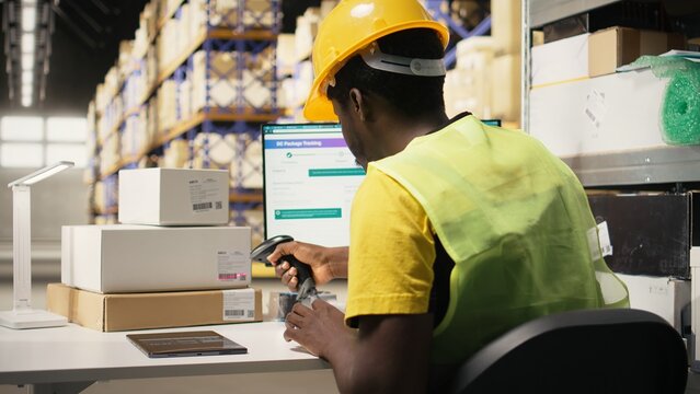 Storage room employee scanning shipping labels to register in inventory, updating records in warehouse management system on pc. Retail e-commerce delivery operations in industrial space. Camera A.