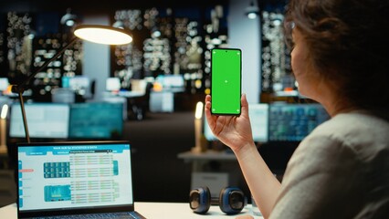 Businesswoman looking at green screen on mobile phone during late night work session, finishing...