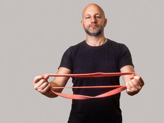 Athletic man in his 40s or 50s holding red resistance band. Male model wearing black shirt with...