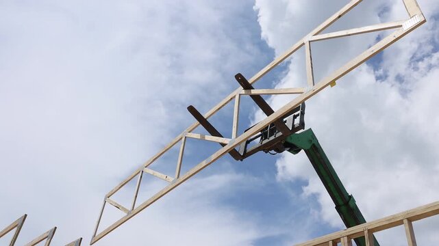 Crane lifts wooden trusses beams to construct building frame during install roofing joins