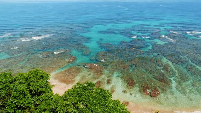 Shallow coastal waters with coral patterns in turquoise ocean under sunny sky