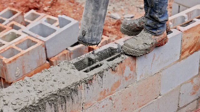 Worker uses concrete mixer to fill wet cement to cinder blocks on construction site