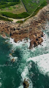 Aerial view toward rocky coast with waves, parked van and red couch, Ancora, Portugal, vertical video