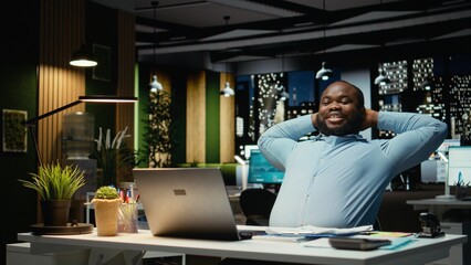Fulfilled black businessman enjoys a quiet moment of downtime in modern office, reclining in desk chair with a comfortable and laid back posture. Resting after tasks, empowerment.