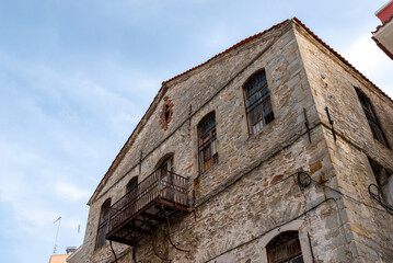 Fototapeta premium Old stone building with small balcony and shuttered windows photographed from low angle, showcasing traditional architecture and textured facade