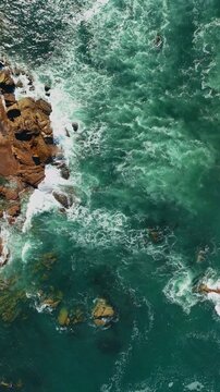 Birds eye view above ocean rocks with waves and white foam, Ancora, Portugal, vertical video