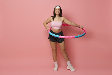 Happy woman training with hula hoop on pink background