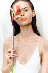Young woman with tropical flower, showcasing natural beauty in minimalistic style, bright colors, and serene expression.