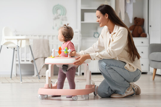Cute little baby girl with walker and her mother in nursery