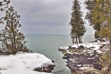 The view of a placid Lake Michigan beyond snow-covered rocky cliffs on a cloudy Winter day at Cave Point County Park in Door County, Wisconsin.