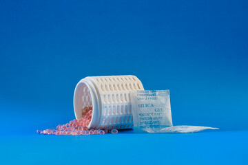 Pink silica gel desiccant beads and moisture absorber packet on vibrant blue background.
