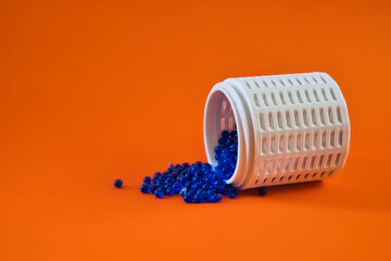 Blue silica gel beads spilling from a white desiccant container on orange background