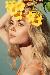 Young woman with flowing blonde hair adorned with vibrant yellow flowers, exuding a serene emotion against a soft green background.