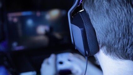 Over-the-Shoulder View of Man Wearing Headphones Playing First-Person Shooter Game on Laptop - Powered by Adobe