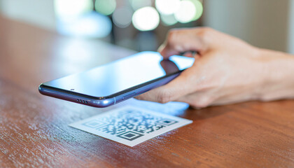 Hand holding smartphone scanning QR code on wooden table indoors with blurred background
