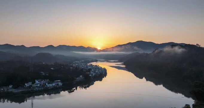 Sunrise time-lapse of over the Xin'an River in Huangshan city, Anhui province, China. Misty mountains, serene waters, and traditional villages reflect in the calm river at dawn.