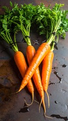 Bunch of vibrant orange carrots with green tops lying on a dark, textured surface