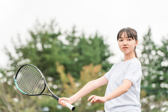 Elementary school, junior high school, and high school girls in gym clothes playing tennis in the schoolyard or on the grounds