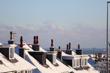 Snowy Rooftops Over a Coastal Town With Chimneys Under Clear Blue Sky