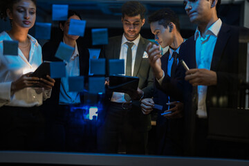 Corporate marketing team planning business growth strategy. Executives analyzing financial goals and market trends using sticky notes on glass wall in modern office.