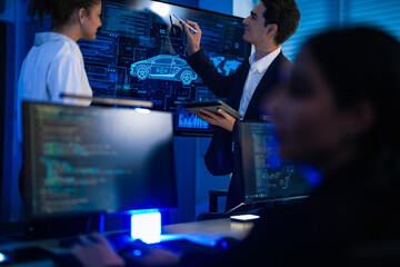 Automotive engineer presenting electric car design on large digital screen. Technical team analyzing vehicle aerodynamics and engine performance data in high-tech laboratory.