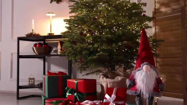 Beautiful Christmas tree with twinkling lights, gift boxes and other festive decor indoors. Camera moving forward