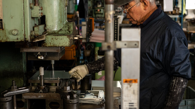 Senior factory worker operating industrial press machine with safety light curtain in manufacturing workshop