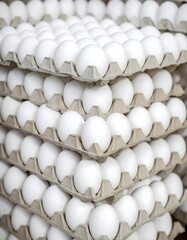 Obraz premium Large number of white eggs in a pyramidal structure on stacked cardboard trays, designed for transport and storage, creating a striking and orderly geometric composition.