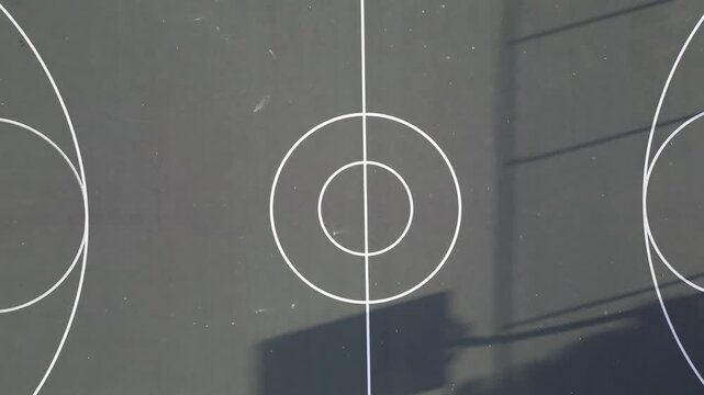basketball court filmed from above (drone view looking down) green surface lines bball afternoon sun long shadows tropical hawaii public park nobody empty hoop center circle basket ball team sports
