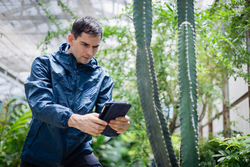 Young scientist in farm greenhouse is part of agricultural research team using tablet to study cactus plants and gather data for innovative farming techniques