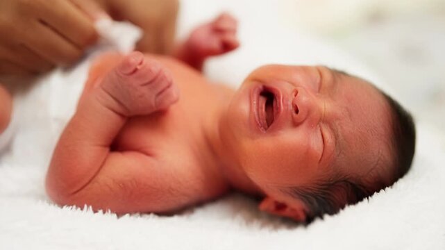 A newborn baby cries loudly after a bath, showing the raw vulnerability and deep emotional connection during early caregiving.