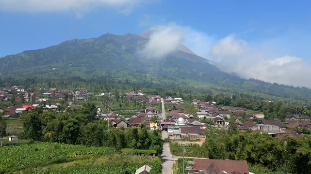 Aerial view of rural village with traditional houses and road leading toward Mount Merapi volcano in Central Java, Indonesia. Scenic landscape showing everyday life near an active volcano.