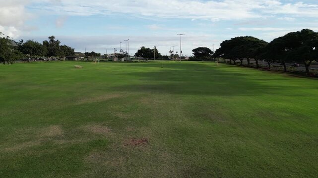 flying over football field with yellow uprights (american touchdown) rural tropical public park in lahaina hawaii (goal scoring green grass) empty nobody team sports game fun athletics high school sky