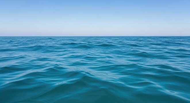 A vast expanse of calm, blue ocean with gentle waves and a clear, blue sky in the background. - Powered by Adobe