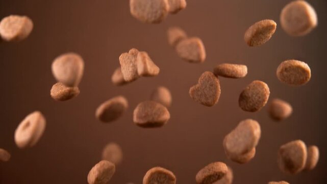 Tiny sweet crunchy brown cookie pieces in assorted fun shapes falling through the air in a studio setting with soft lighting