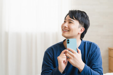 ベッドの上でスマートフォンを操作する若い男性　ライフスタイルイメージ