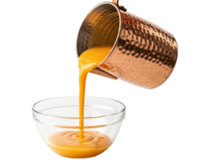 Hammered copper pot pouring orange pumpkin soup into glass bowl isolated on transparent background