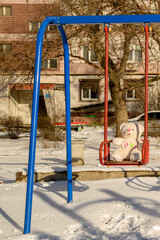 soft teddy bear on a swing at a snowy playground